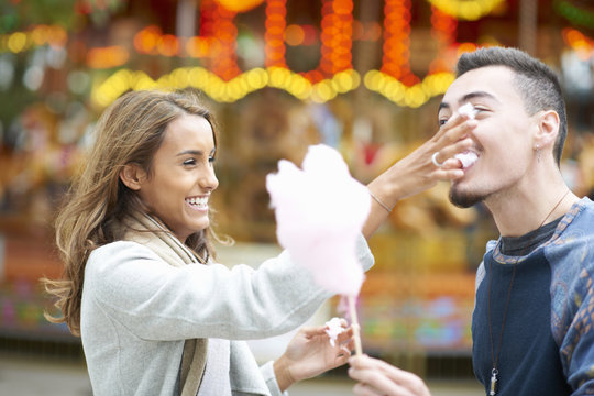 Young couple, fooling around, eating candy floss at funfair, outdoors