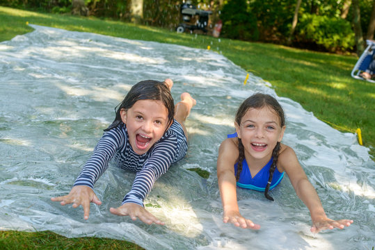 Two girls sliding on slip n slide water mat in garden