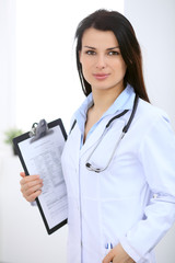 Brunette female doctor on the background of colleagues talking to each other in hospital