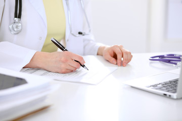 Close-up of a female doctor filling  out application form , sitting at the table in the hospital
