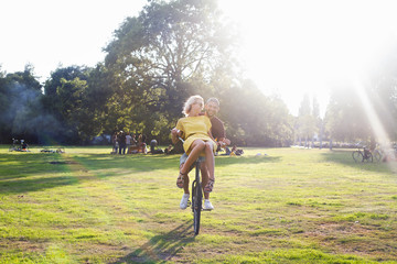 Young couple having fun on bicycle at sunset party in park