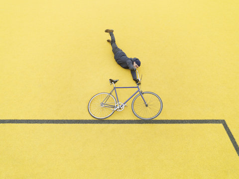 Urban cyclist doing illusionary stunt against yellow wall