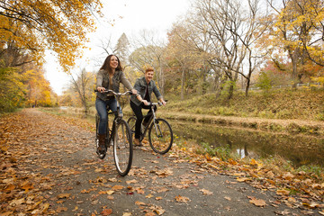 Happy young couple cycling along riverside in autumn