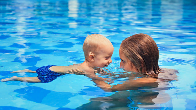 Happy little sports man with mother - active baby swim with fun in woman hands in swimming pool. Swimming people, family lifestyle and summer children water activity and swimming lesson with parents.