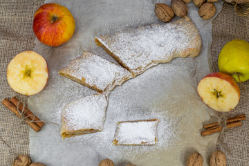 Fototapeta na wymiar Sugared Homemade Apple Strudel on a Baking Paper, Walnut, Cinnam
