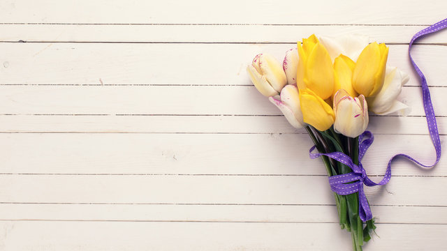 Bright yellow and white spring tulips on white wooden background