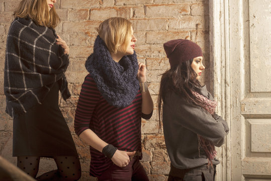 Side view of women wearing knitwear standing on stairs in front of brick wall looking away