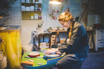 Side view of young woman sitting in workshop using potters wheel, looking down smiling
