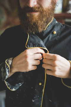 Cropped view of bearded mid adult man buttoning up clay covered jacket