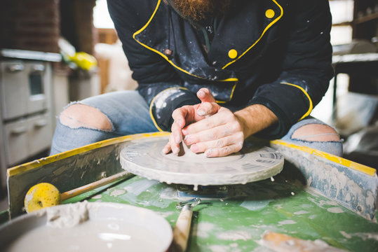 Cropped front view of mid adult man shaping clay on pottery wheel