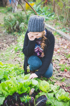 Young woman crouching in vegetable patch checking lettuce, using cellular phone smiling
