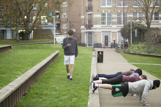 Group of adults exercising outdoors, young man looking at stopwatch