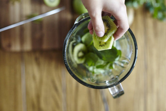 Woman holding sliced green kiwi over blender