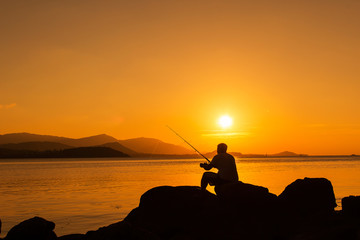 Young man sitting on stone fishing at sea sunset backgroung