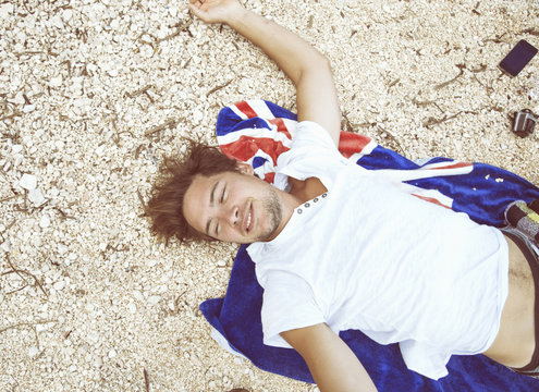 Overhead view of young man lying on back on beach on beach towel, looking away smiling,Sardinia, Italy