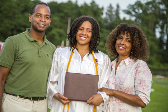 Portrait of teenage girl with parents at graduation ceremony