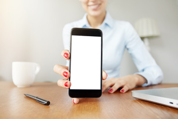 Cropped shot of cute smiling female office worker in white shirt showing funny pictures on cell phone with blank copy space screen for your text or advertising content. Selective focus, film effect