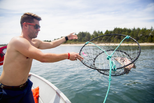 Mid adult man throwing baited crab trap from fishing boat, Nehalem Bay, Oregon, USA