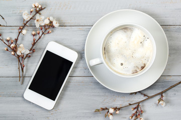 Cup of coffee and smartphone on wooden table with cherry flowers, top view