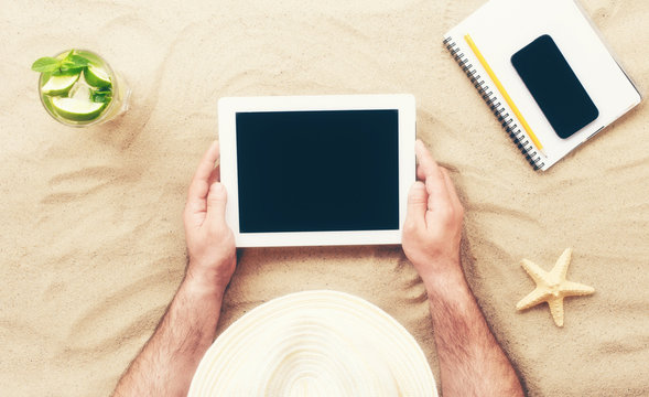 Man holding tablet with blank screen lying on the beach