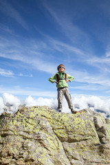 The six years boy stands on top of big rock in mountains