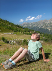 The smiling boy sits on slope in european mountains