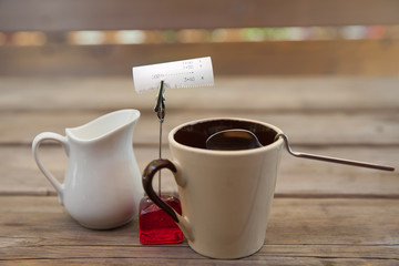 A milk jug and a cup of black coffee on a wooden table with bill