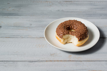Bitten donut on a plate on a wooden background