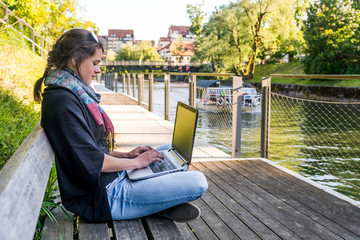 Young woman using laptop at a riverbank.
