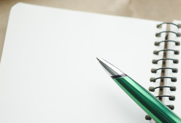 A part of open blank white notebook and green pen on the desk