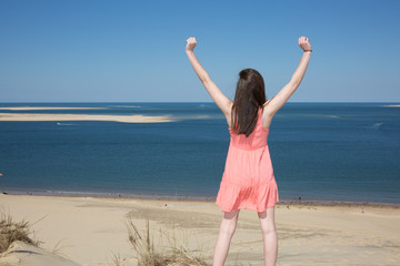 Happy woman enjoying relaxing breeze and freedom by the sea. Joyful asian girl raising arms to the sky.