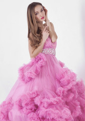 Fototapeta premium Portrait of young beautiful caucasian blonde in gorgeous pink dress on white background