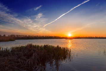 sunset over a swamp lake trail aircraft in the sky.