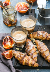 Traditional Italian style home breakfast. Latte in glasses, almond croissants and red bloody Sicilian oranges over concrete textured table