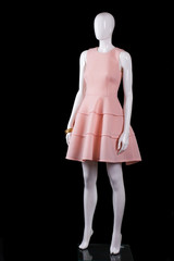 Sleeveless salmon dress with folds. Salmon dress on white mannequin. Stylish mannequin on black background. Trendy garment with golden accessory.