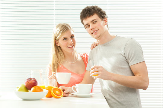 Young casual couple have breakfast with coffee and fruit with venetian blind window