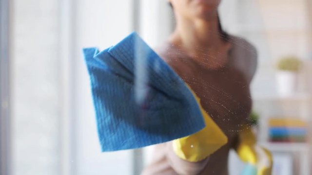 woman in gloves cleaning window with rag and spray