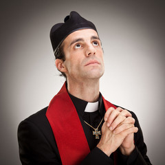 young cristian catholic priest with crucifix pray portrait on grey background