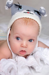 Little boy in a funny wool hat with mug animal on white sheet