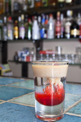 Monkey-brain cocktail in a shot glass on blue tiled bar - table in a cafe.