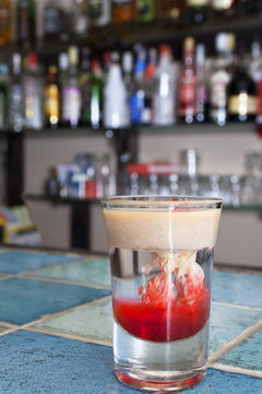 Monkey-brain cocktail in a shot glass on blue tiled bar - table in a cafe.