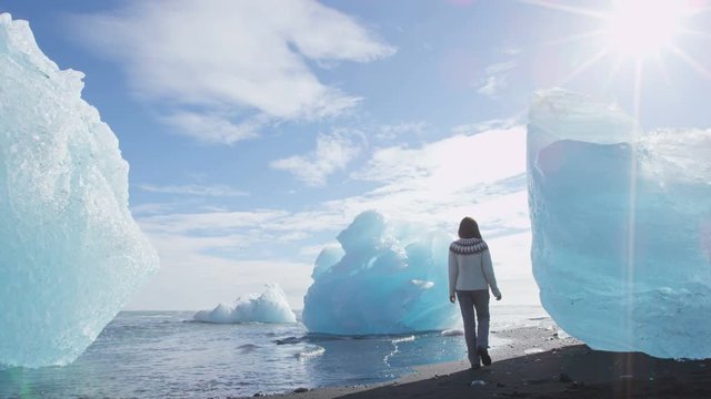 Iceland Jokulsarlon Iceberg beach. Tourist walking by icebergs on Ice beach. Breidamerkursandur beach by jokulsarlon glacial lagoon / glacier lake nature landscape. Woman. RED EPIC, SLOW MOTION.