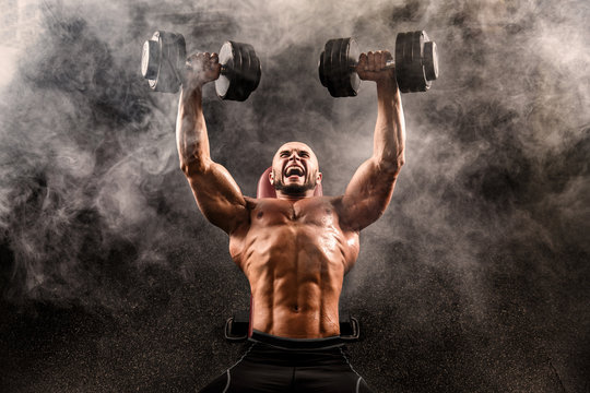 Topless muscular man doing dumbbell exercise on bench press