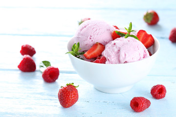 Ice cream in bowl with strawberries and raspberries on blue wood