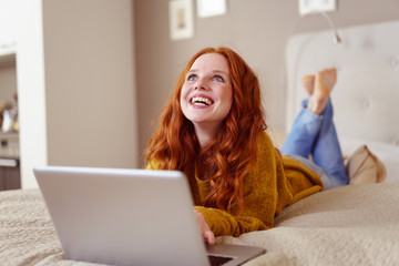 frau liegt auf dem bett mit ihrem laptop und schaut lachend nach oben