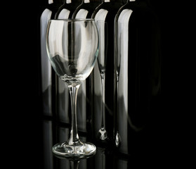 Glass and wine bottles in a row on black  background, close up
