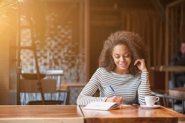 Cheerful young woman is writing in notebook - Powered by Adobe