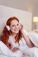 Naklejka premium frau liegt im bett und hört musik mit ihrem mobiltelefon