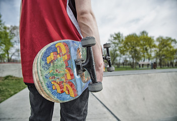 Skater boy standing back to camera holding skateboard, grunge styled