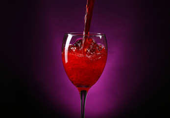 Wine pouring in glass on dark purple background